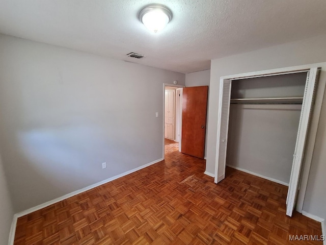 unfurnished bedroom featuring dark parquet floors, a textured ceiling, and a closet