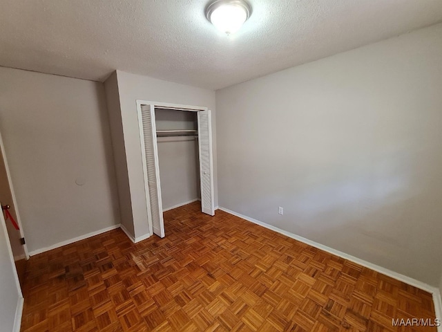 unfurnished bedroom featuring a closet, a textured ceiling, and dark parquet flooring