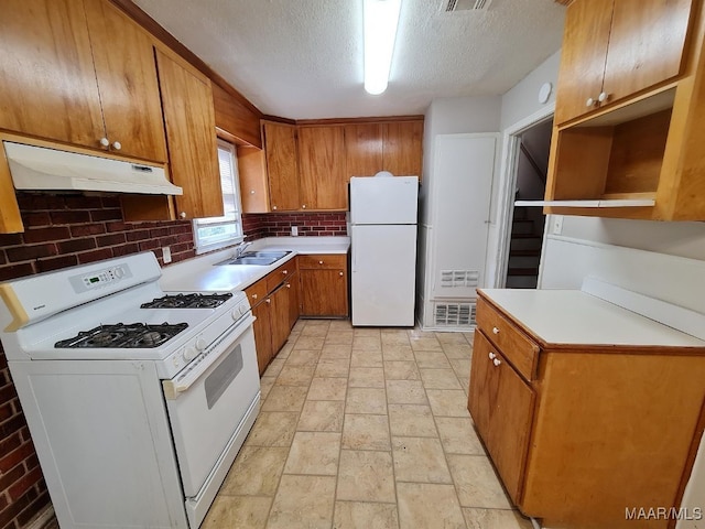 kitchen featuring white appliances, under cabinet range hood, brown cabinets, a sink, and a textured ceiling