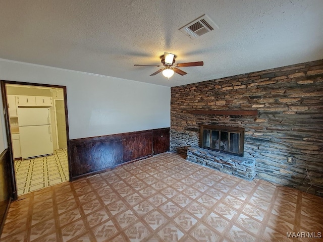 unfurnished living room featuring wood walls, ornamental molding, a textured ceiling, a fireplace, and ceiling fan