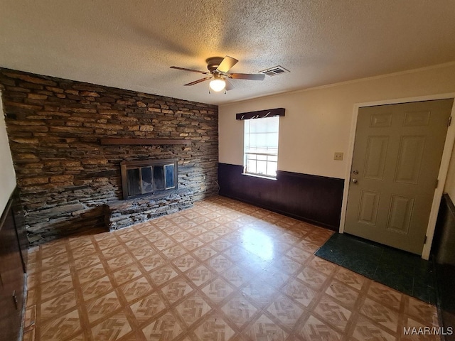 unfurnished living room featuring wood walls, a stone fireplace, a textured ceiling, ceiling fan, and ornamental molding