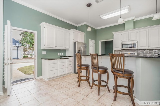 kitchen with stainless steel appliances, dark countertops, white cabinets, and ornamental molding