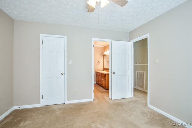 unfurnished bedroom with a textured ceiling, ensuite bath, light colored carpet, and ceiling fan