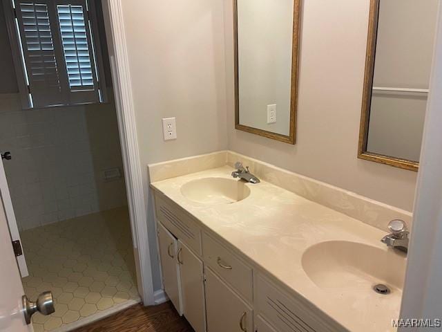 bathroom with a tile shower, double vanity, and a sink