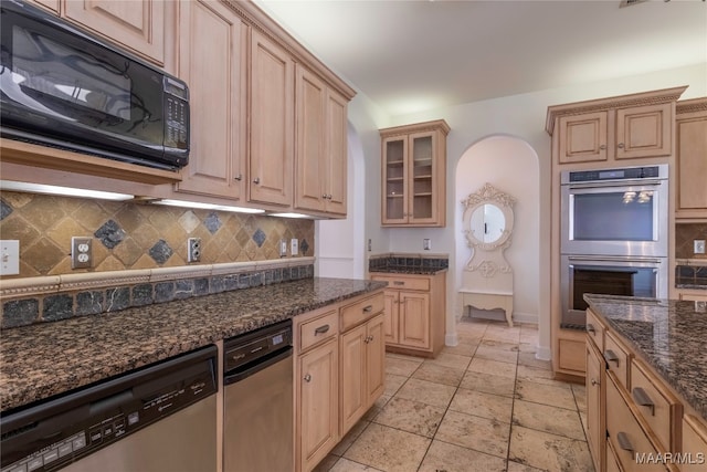 kitchen featuring appliances with stainless steel finishes, light brown cabinetry, decorative backsplash, and dark stone counters