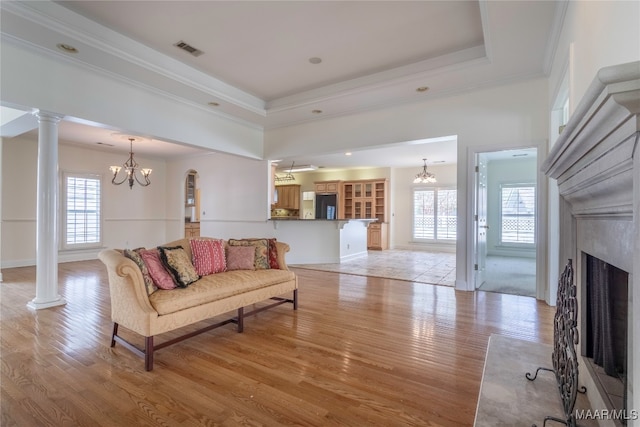 living room with crown molding, a tray ceiling, light hardwood / wood-style floors, a chandelier, and ornate columns