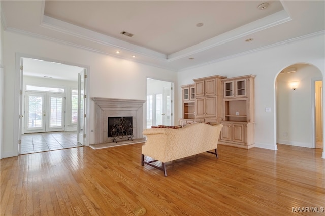 unfurnished living room with french doors, ornamental molding, a raised ceiling, a fireplace, and light hardwood / wood-style floors