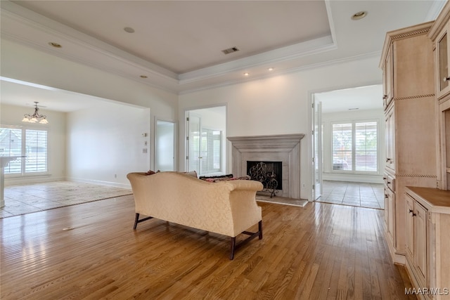 living room with ornamental molding, plenty of natural light, a raised ceiling, and light hardwood / wood-style flooring