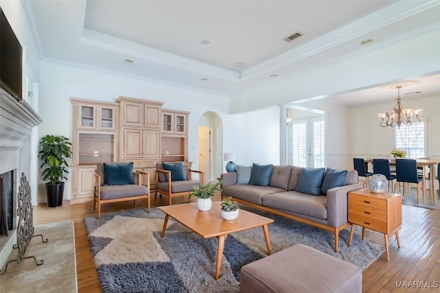 living room with an inviting chandelier, ornamental molding, a raised ceiling, and light hardwood / wood-style flooring