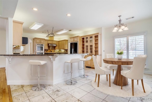 kitchen with black refrigerator, pendant lighting, a breakfast bar, dark stone countertops, and kitchen peninsula