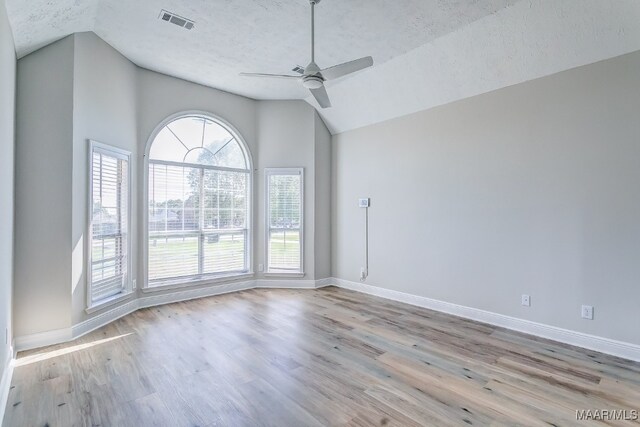 unfurnished room with ceiling fan, a textured ceiling, lofted ceiling, and light wood-type flooring