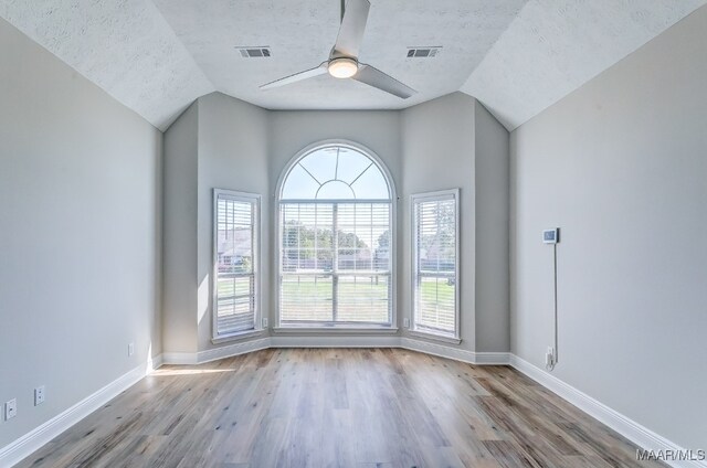 empty room featuring lofted ceiling, a textured ceiling, and light hardwood / wood-style floors