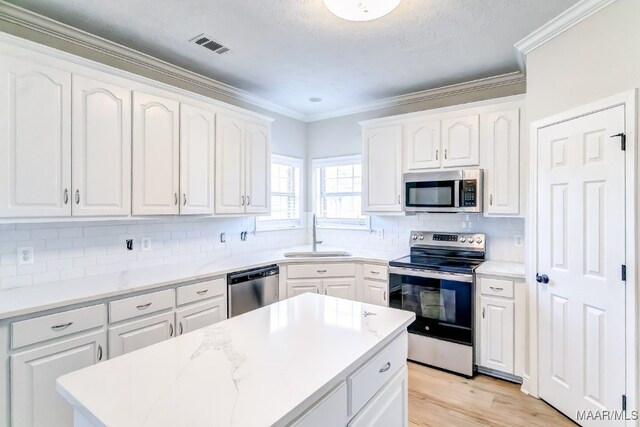 kitchen featuring decorative backsplash, appliances with stainless steel finishes, white cabinetry, crown molding, and sink