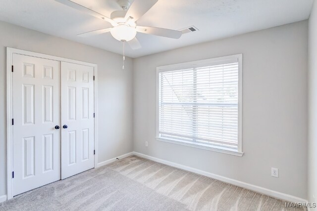 unfurnished bedroom with a closet, light colored carpet, and ceiling fan