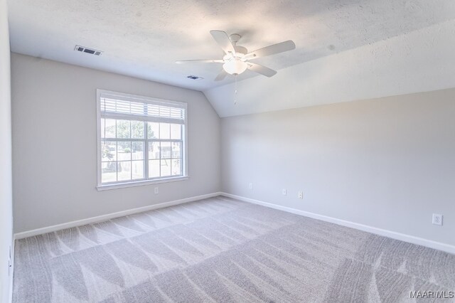 empty room featuring a textured ceiling, ceiling fan, carpet, and vaulted ceiling