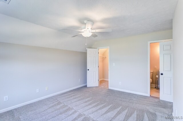 unfurnished bedroom with connected bathroom, a closet, a walk in closet, light colored carpet, and ceiling fan