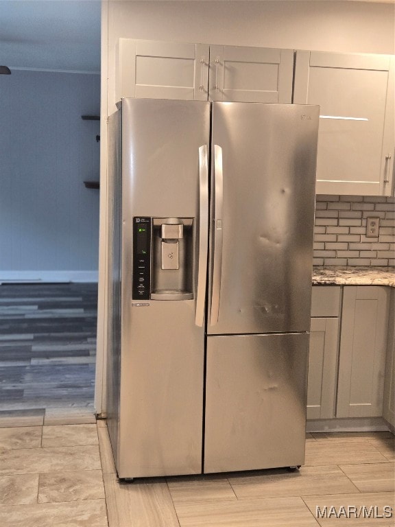 kitchen featuring light hardwood / wood-style floors, stainless steel fridge, light stone counters, and backsplash