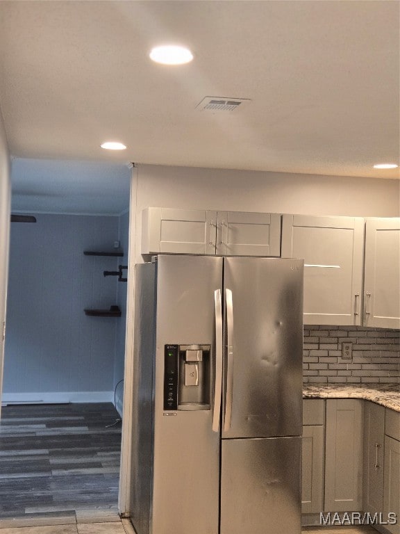 kitchen with decorative backsplash, light stone counters, dark wood-type flooring, and stainless steel fridge with ice dispenser