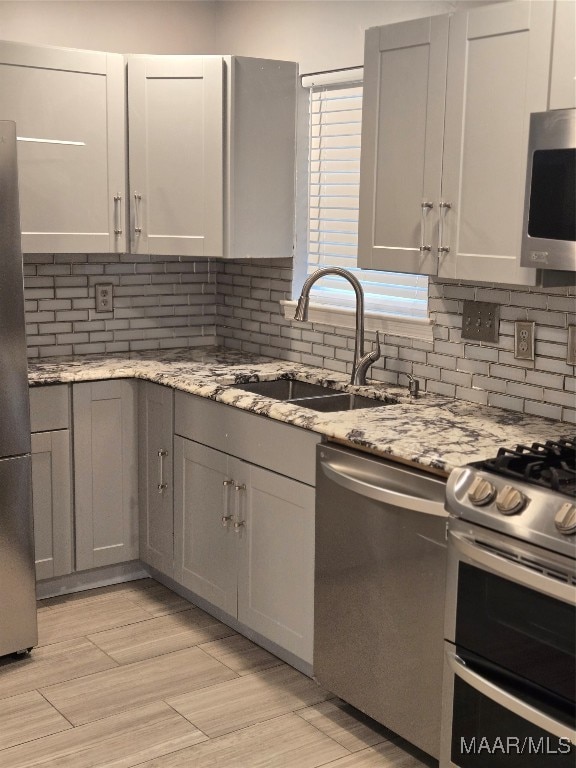 kitchen featuring light stone countertops, appliances with stainless steel finishes, sink, and backsplash