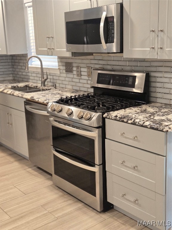 kitchen with tasteful backsplash, light stone countertops, sink, white cabinetry, and stainless steel appliances