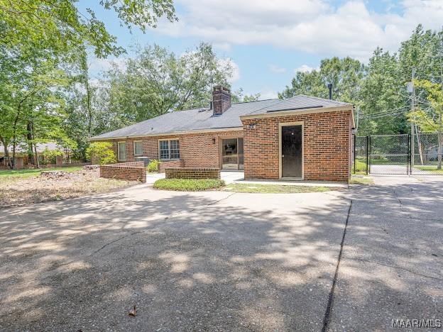 rear view of house with concrete driveway, a chimney, a gate, fence, and brick siding