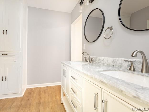 full bathroom with double vanity, wood finished floors, baseboards, and a sink