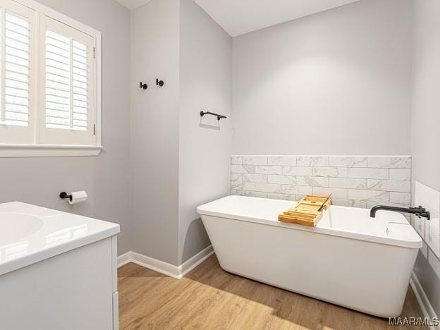 bathroom with wood finished floors, vanity, a freestanding bath, and tile walls