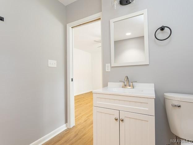 bathroom featuring toilet, vanity, wood finished floors, and baseboards