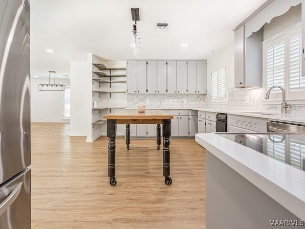 kitchen with a sink, tasteful backsplash, visible vents, light wood-style flooring, and appliances with stainless steel finishes