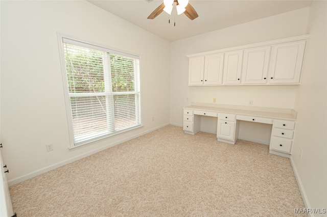 unfurnished office with built in desk, ceiling fan, and light colored carpet