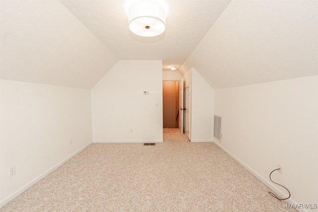 additional living space with a textured ceiling, vaulted ceiling, and light colored carpet