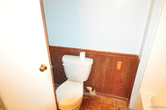 bathroom featuring tile patterned flooring, toilet, a tub, and wooden walls