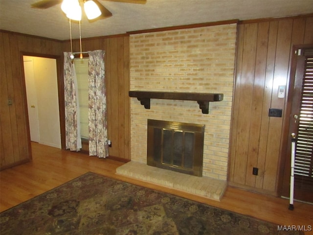 living room with wood walls, wood-type flooring, a brick fireplace, ceiling fan, and crown molding