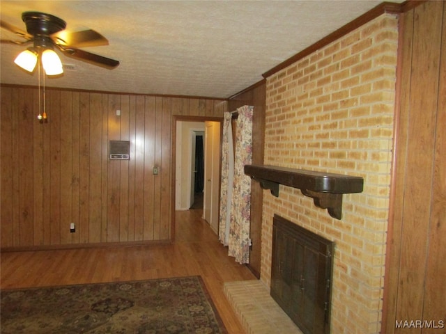 living room with a fireplace, wooden walls, a textured ceiling, light hardwood / wood-style floors, and ceiling fan