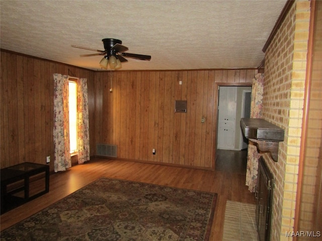 living room featuring hardwood / wood-style floors, ceiling fan, a brick fireplace, and wood walls