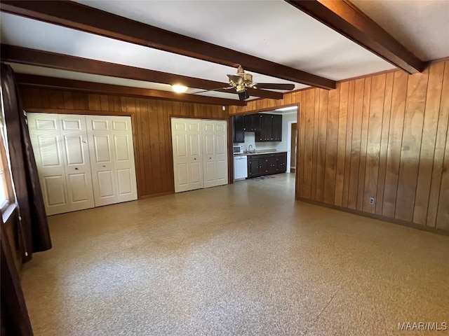 unfurnished living room featuring wood walls, beamed ceiling, sink, and ceiling fan