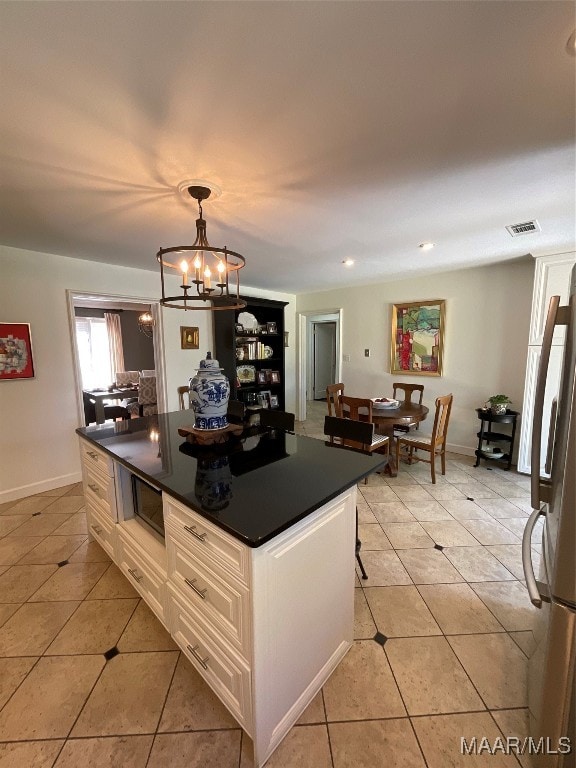 kitchen featuring light tile patterned flooring, refrigerator, hanging light fixtures, white cabinets, and an inviting chandelier