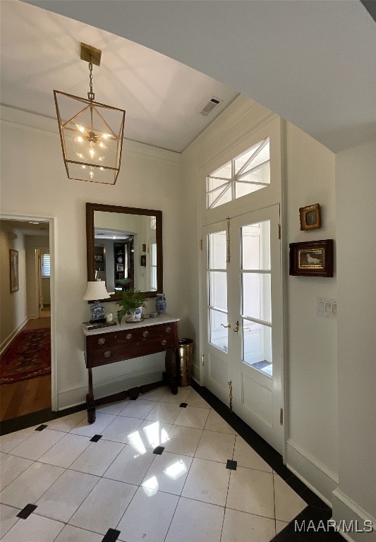 doorway with an inviting chandelier, french doors, ornamental molding, and light tile patterned floors