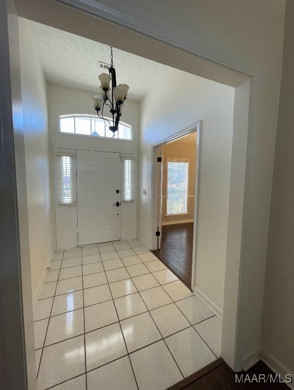 tiled foyer featuring a textured ceiling, a chandelier, and plenty of natural light