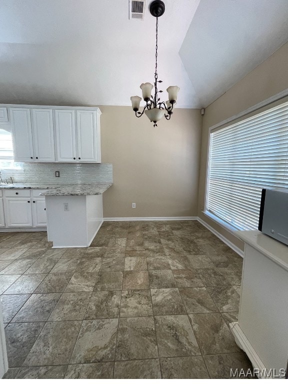 kitchen featuring a wealth of natural light, vaulted ceiling, decorative light fixtures, and white cabinets