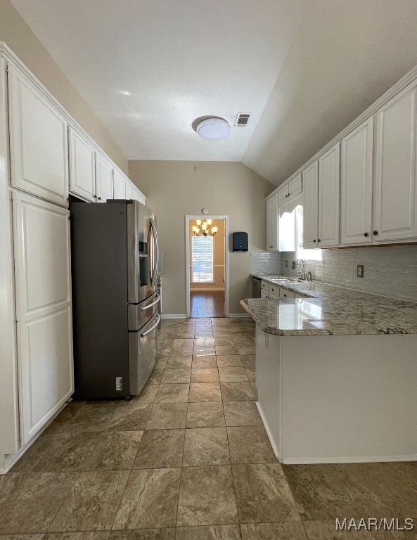 kitchen with light stone countertops, kitchen peninsula, stainless steel fridge, vaulted ceiling, and white cabinets