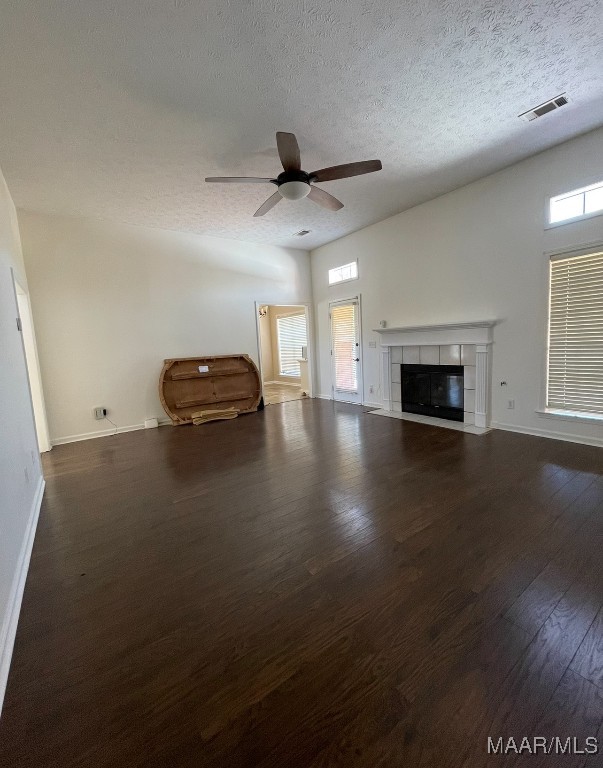 unfurnished living room featuring dark hardwood / wood-style floors, a textured ceiling, a tile fireplace, and ceiling fan