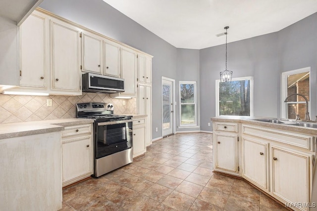 kitchen with sink, hanging light fixtures, cream cabinetry, stainless steel appliances, and backsplash