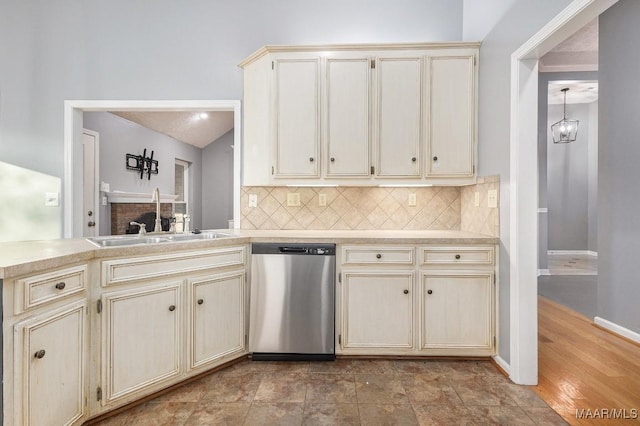 kitchen with lofted ceiling, sink, decorative backsplash, stainless steel dishwasher, and cream cabinetry