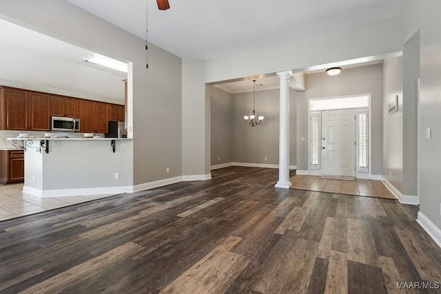 entryway with decorative columns, wood-type flooring, and an inviting chandelier