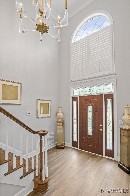 foyer featuring a towering ceiling, crown molding, a chandelier, and light wood-type flooring