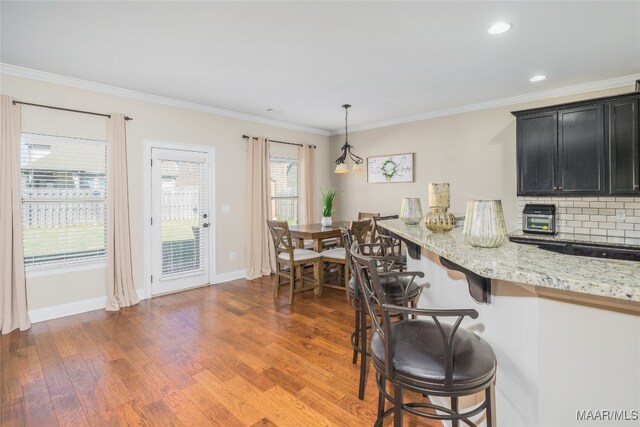 kitchen with dark hardwood / wood-style floors, a breakfast bar, light stone countertops, decorative light fixtures, and tasteful backsplash