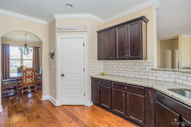 kitchen featuring dark hardwood / wood-style flooring, ornamental molding, dark brown cabinetry, decorative backsplash, and an inviting chandelier