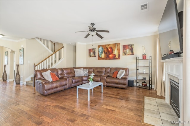 living room featuring ornamental molding, wood-type flooring, a tile fireplace, and ceiling fan