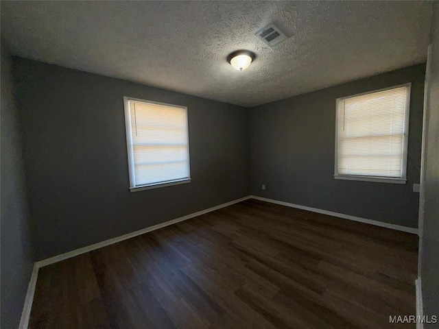 spare room with a textured ceiling and dark hardwood / wood-style flooring